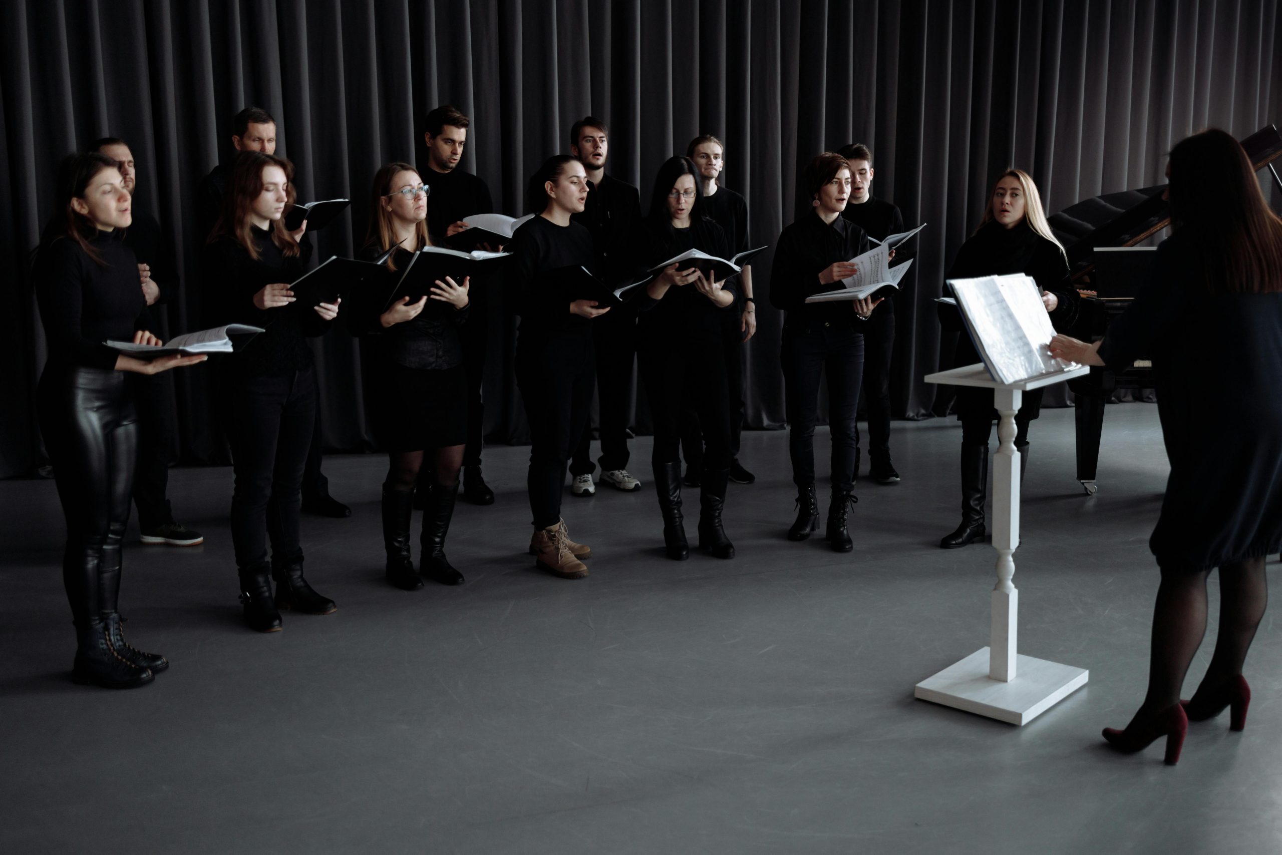 A choir group rehearsing with music sheets under a conductor's direction indoors, focusing on harmony.